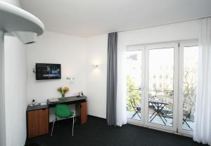 Zimmer mit einem Schreibtisch mit einem grünen Stuhl und einem Balkon. in der Unterkunft Chelsea Hotel in Köln