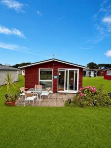 a red house with a table and chairs in a yard at The Coastal Cosy, St Merryn, Padstow in Saint Merryn