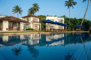 a house with a swimming pool with blue umbrellas at Kumu Beach By Teardrop Hotels in Balapitiya