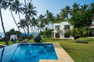 a pool in front of a house with palm trees at Kumu Beach By Teardrop Hotels in Balapitiya