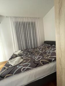 a bed with a black and white comforter and a window at Anya Apartman - self check in in Čačak