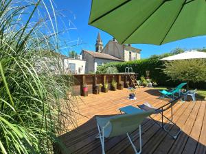 a patio with a green umbrella and chairs on a deck at Chambres d'hôtes Ecole Buissonnière en Dordogne in Le Buisson de Cadouin
