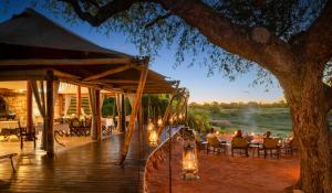 a wooden deck with people sitting at tables under a tree at Onguma Tented Camp in Mokuti Lodge +5 photos