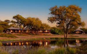 a lodges with their lights on next to a body of water at Onguma Tented Camp in Mokuti Lodge