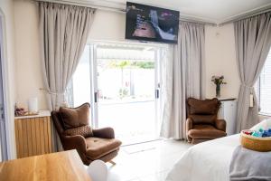 a bedroom with a bed and two chairs and a sliding glass door at @47 Guest House in Gqeberha