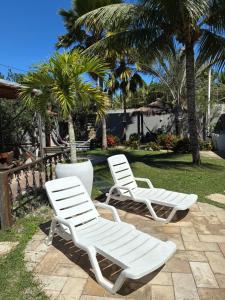 two white lounge chairs sitting on a patio with palm trees at Pousada Sapê in Praia do Frances