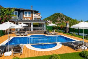 a pool with chairs and umbrellas in front of a house at Villa Delfin in Ortaca