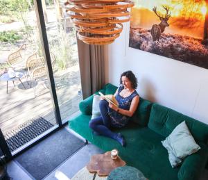 a woman sitting on a couch reading a book at Tiny House of Happiness - shared hot tub in Otterlo