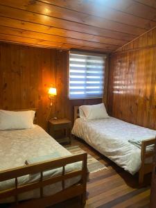 two beds in a room with wooden walls at Cabañas Puchuman Lican Ray in Licán Ray