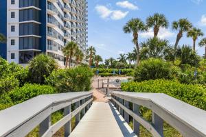 a boardwalk over the beach with palm trees and a building at Sunny beachfront condo with pool and SW-facing balcony in Marco Island