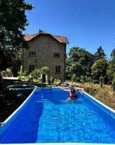 a woman in a swimming pool in front of a building at Bon Chez Nous in Saint-Amand-Jartoudeix