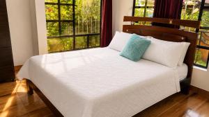 a bed with white sheets and blue pillows in a room with windows at Finca cuatro orquídeas in La Mesa