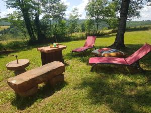 two chairs and a table and a bench in the grass at Maison d'hôtes en grès rouge in Lanteuil