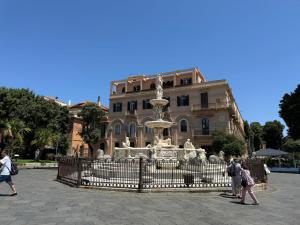 a fountain in front of a building with people walking by it at BellDuomo Suite Messina in Messina