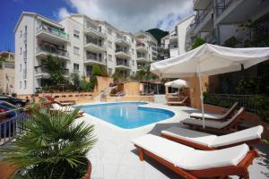 a swimming pool with chairs and an umbrella and some buildings at Apartmani Bozenov in Petrovac na Moru