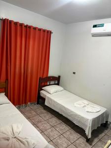 two beds in a room with a red curtain at Hotel em Caçu in Caçu