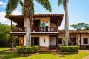 two people standing on the balcony of a house with palm trees at Hotel Finca Buenos Aires Barichara in Barichara