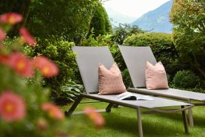 two white chairs with pillows sitting on the grass at Appartement Karnutsch in Schenna