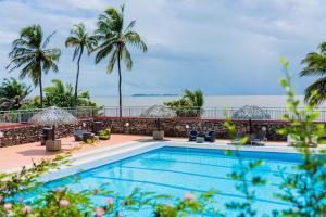 a pool with palm trees and the ocean in the background at Hôtel des Roches Kourou in Kourou