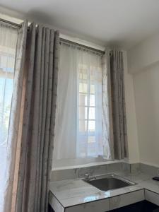 a kitchen with a sink and a window with curtains at Stlounge-kisaju in Stony Athi