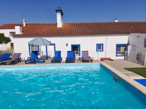 a swimming pool with blue chairs and a white building at Alojamento local A Giesta in Sao Sebastiao da Giesteira
