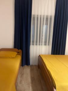 a room with two beds and a window with blue curtains at Guest House Vuthaj in Vusanje