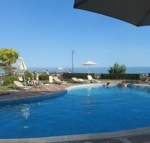 a swimming pool with people sitting in chairs and the ocean at Apartment Caricia complex Carpe Diem Balchik - sea view & free parking in Balchik