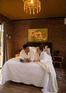 two people sitting on a bed in a bedroom at Chalés Manacá dos Canyons in Praia Grande