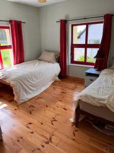 two beds in a bedroom with red curtains and a wooden floor at Callacoon Cottage in Louisburgh