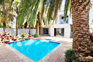 a swimming pool in front of a house with palm trees at Magic garden in Vereeniging