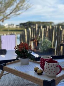 a table with two coffee cups and a vase with flowers at Refúgio do Lago in Linhares