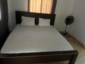 a bed with white sheets and pillows and a fan at The Senegambia Hideaway in Amdalai
