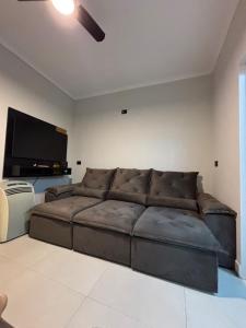 a living room with a brown couch and a flat screen tv at Sussurros do Mar in Bertioga