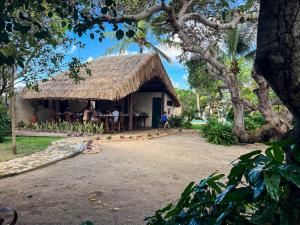 a house with a thatched roof with people sitting at a table at Pousada Estação Cajueiro in São Miguel do Gostoso