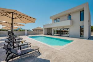 a villa with a swimming pool with chairs and an umbrella at Nimar Villas in Gaïtánion