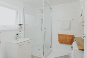 a white bathroom with a shower and a sink at Warm & Cosy Studio Cabin in Hamilton +11 photos