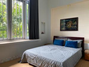 a bedroom with a bed with blue pillows and windows at Một Phòng Trong Villa View Sân Vườn, Hồ Bơi in Ấp Phú Khương