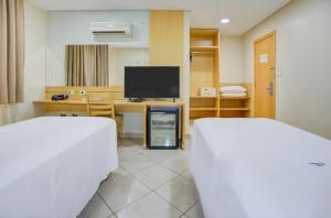 a room with two beds and a desk with a television at Hotel Domani in Guarulhos