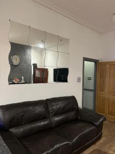 a leather couch in a living room with a clock on the wall at Haven Home 3 bedrooms near Sunderland City Centre Downstairs Shower with Toilet and Upstairs Bath with Toilet TV in each room in Sunderland