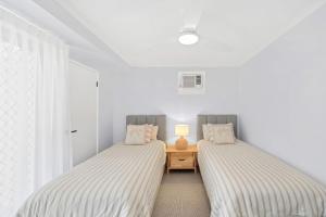 two beds in a room with white walls and a table at Beach Street - Town Location - Stone Real Estate Yamba in Yamba
