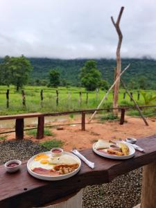 two plates of breakfast food on a wooden table at Cow Barn Cafe and Lodge Preah Vihear in Phumĭ Nhông
