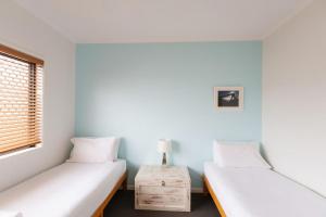 two twin beds in a room with a table at Six River - Town Location - Stone Real Estate Yamba in Yamba