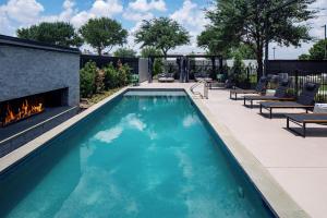 an outdoor pool with a fireplace and lounge chairs at The Clara Hotel Plano, Tapestry Collection by Hilton in Plano