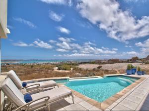 a swimming pool with chairs and the ocean in the background at Dunestone Boutique GuestHouse in Langebaan