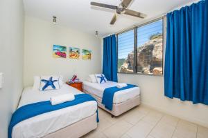 a bedroom with two beds with blue curtains and a window at 1 Bright Point Apartment 5301 in Nelly Bay