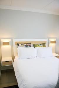 a bed with white sheets and pillows next to two lights at White Orchid Luxury Apartment in Chartwell