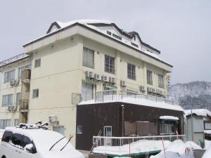 un edificio cubierto de nieve con un coche aparcado delante de él en Kadowakikan, en Nozawa Onsen