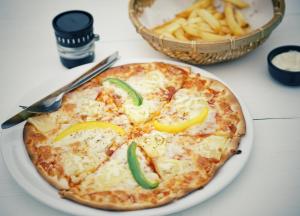 a pizza with peppers and cheese on a plate with a basket of fries at Cookies Salad Resort in Salad Beach