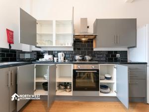 a kitchen with grey and white cabinets and appliances at Leigh 2-Bedroom House Near Haydock & Wigan in Leigh