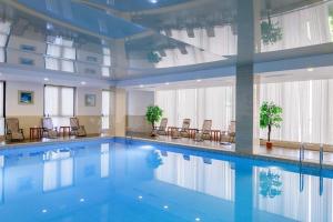 a large swimming pool in a building with chairs at Shera Inn Hotel in Almaty